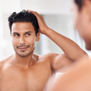Hombre con pelo mirandose al espejo despues de haber superado un tratamiento en implante de pelo con los cuidados especificos